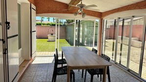A patio with a table and chairs, a ceiling fan, and a view of a garden. - 500 meters from the beach, a 3-bedroom family home with a terrace and barbecue (Agde)