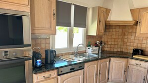 A kitchen with wooden cabinets, a stainless steel oven, a coffee maker, and a sink. - 500 meters from the beach, a 3-bedroom family home with a terrace and barbecue (Agde)