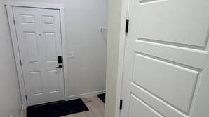 Ein Korridor mit Holzboden, einer weißen Tür mit schwarzem Griff und einer weißen Wand mit Lichtschalter.