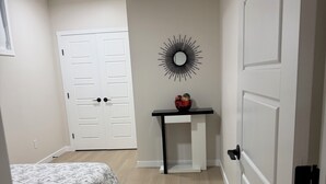 Ein Schlafzimmer mit einem Bett, einer weißen Tür, einem kleinen Tisch mit einer Schale und einem wandmontierten Spiegel.