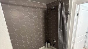 A bathroom with a hexagonal tile wall, a bathtub, a shower curtain, and a door leading to another room. - Luxury stay in heart of W Hollywood with free parking & pool (West Hollywood)