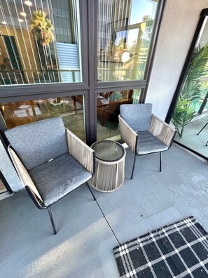 A seating area with two chairs and a small round table, a checkered mat, and a glass wall with reflections.