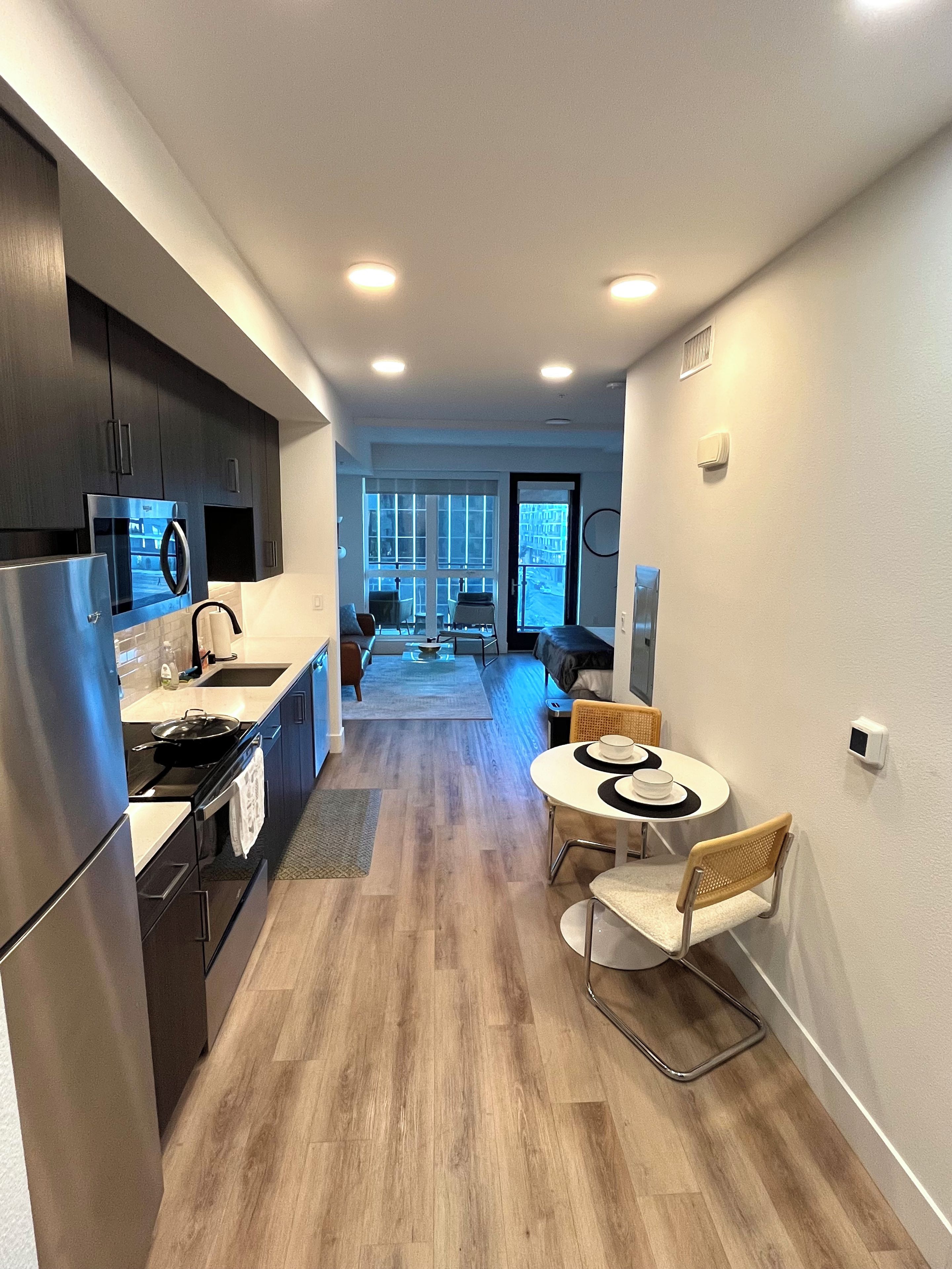 A modern kitchen with dark cabinetry, a stainless steel refrigerator, and a dining area with a round table and chairs.
