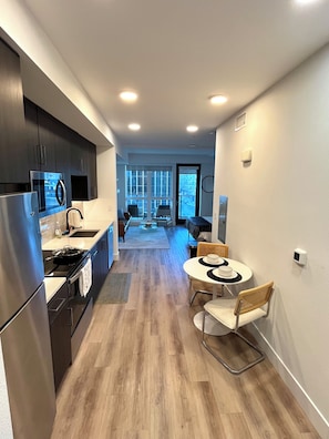 A modern kitchen with dark cabinetry, a stainless steel refrigerator, and a dining area with a round table and chairs.