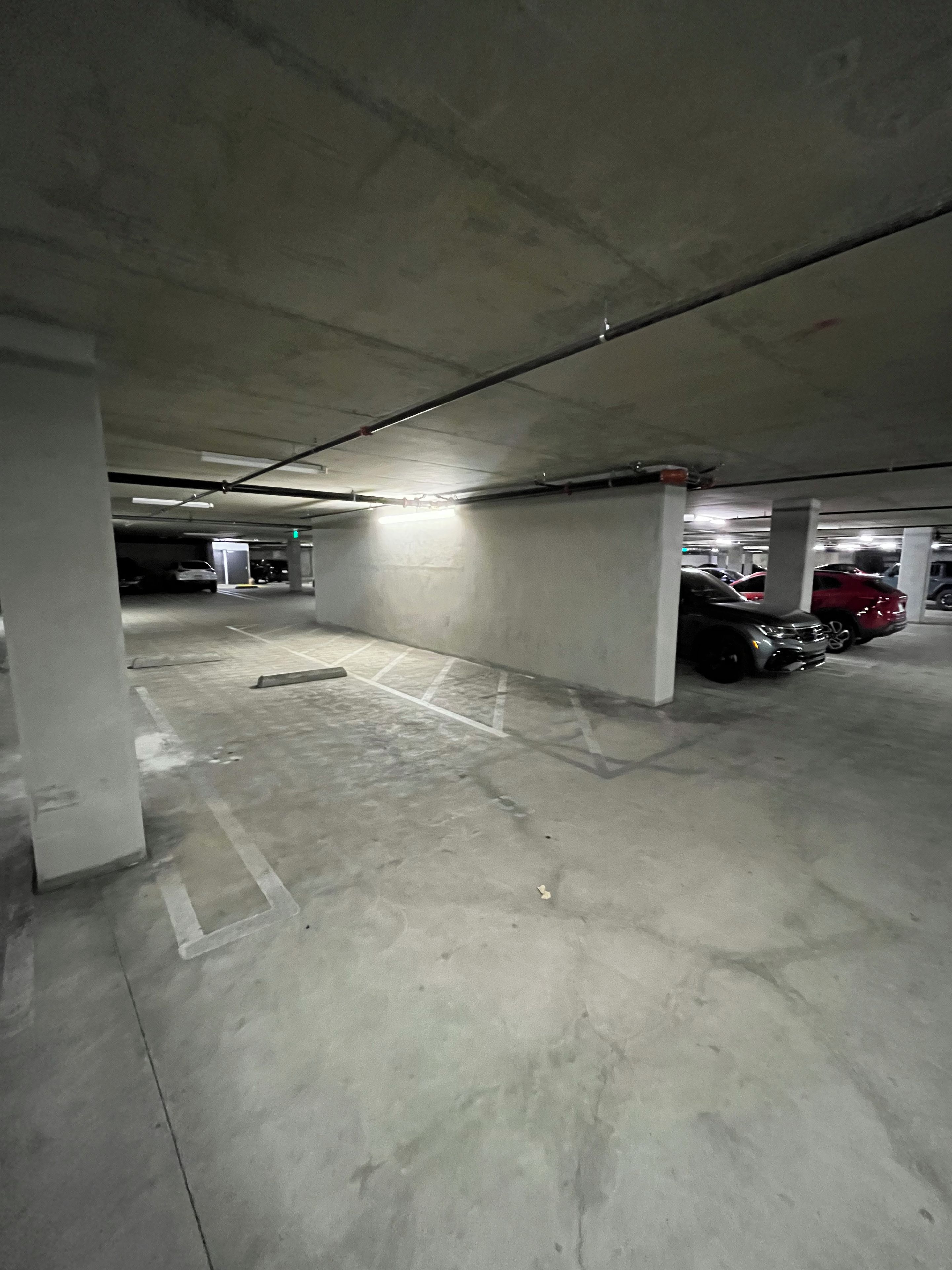 An underground parking garage with concrete pillars, marked parking spaces, and several parked cars.