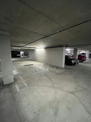 Een ondergrondse parkeergarage met betonnen pilaren, aangegeven parkeerplaatsen en meerdere geparkeerde auto's.