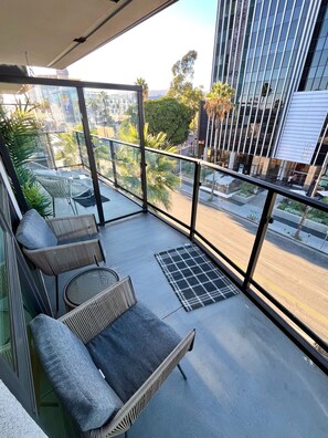 A balcony with wicker furniture, a glass railing, and a view of a cityscape.