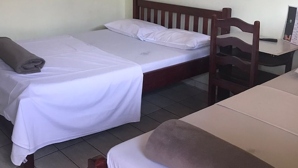 A room with two beds, a wooden chair, a small table, and a wall-mounted light switch. - Hotel Park (Valparaiso de Goias)