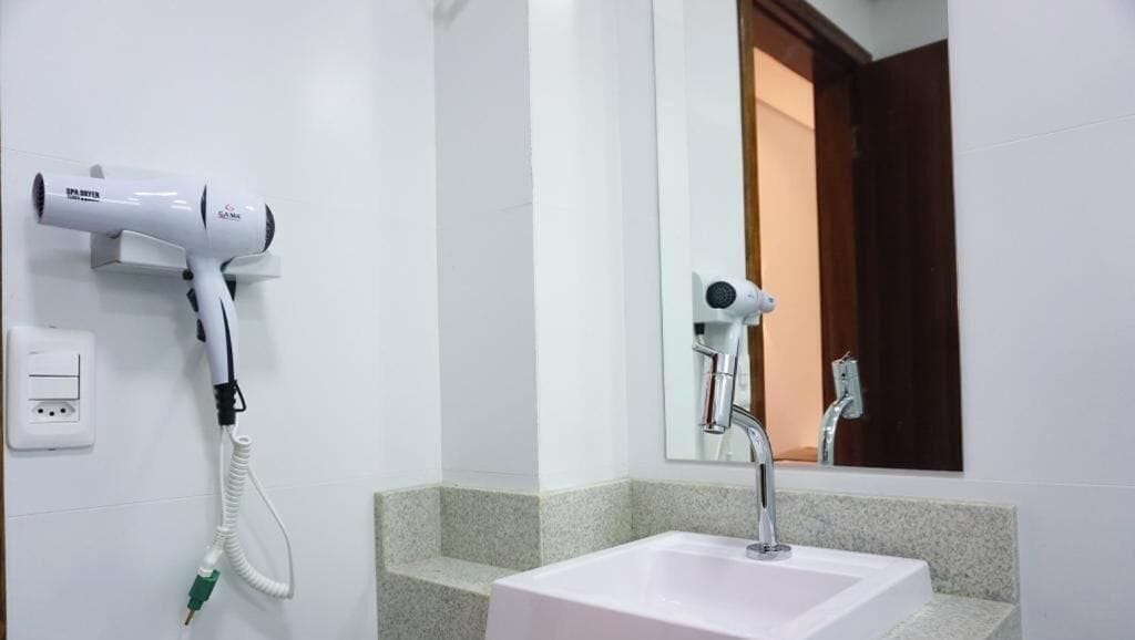 Un baño con un lavamanos blanco, un espejo y dos secadores de pelo montados en la pared.