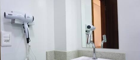 Un baño con un lavamanos blanco, un espejo y dos secadores de pelo montados en la pared.