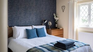 A bedroom with a bed, a bedside table with a lamp, a mirror, and a window with curtains. - Huge Peaceful 3Bed With FREE Parking (West Sussex)