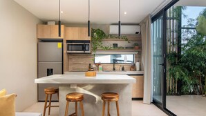 A modern kitchen with a central island, wooden stools, and a view of greenery outside. - Modern Private Estate: 2 Homes, Jacuzzi, Cinema & Volcano Views (FORTUNA)