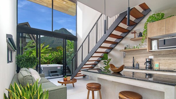 A modern kitchen with a wooden staircase, a bar area, and a seating space with a view of mountains. - Modern Private Estate: 2 Homes, Jacuzzi, Cinema & Volcano Views (FORTUNA)