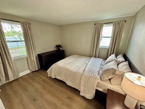 A bedroom with a bed, a nightstand, a lamp, and curtains. - Fully Renovated Coastal Retreat 3BR w/ Garage & Screened Lanai (Apollo Beach)