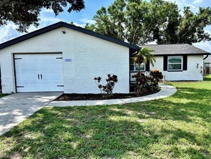 A single-story house with a garage, a number sign, and a well-maintained lawn. - Fully Renovated Coastal Retreat 3BR w/ Garage & Screened Lanai (Apollo Beach)