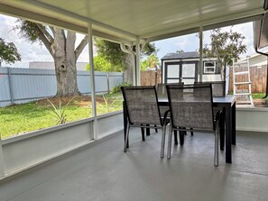 A covered patio area with a table and chairs, a view of the backyard, and a wooden fence. - Fully Renovated Coastal Retreat 3BR w/ Garage & Screened Lanai (Apollo Beach)