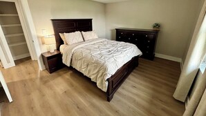 A bedroom with a wooden bed, a nightstand, a dresser, and a walk-in closet. - Fully Renovated Coastal Retreat 3BR w/ Garage & Screened Lanai (Apollo Beach)