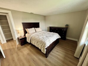 A bedroom with a wooden bed, a nightstand, a dresser, and a walk-in closet. - Fully Renovated Coastal Retreat 3BR w/ Garage & Screened Lanai (Apollo Beach)
