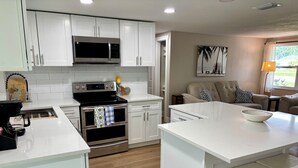 A modern kitchen with white cabinetry, a built-in microwave, a stove, and an oven. There is a dining area with a white table and a bowl on it. - Fully Renovated Coastal Retreat 3BR w/ Garage & Screened Lanai (Apollo Beach)