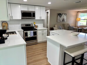 A modern kitchen with white cabinetry, a built-in microwave, a stove, and an oven. There is a dining area with a white table and a bowl on it. - Fully Renovated Coastal Retreat 3BR w/ Garage & Screened Lanai (Apollo Beach)