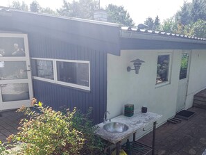 A small, single-story building with a dark exterior, a white door, and a window. - 4 Star Holiday Home in Hundested (Hundested)
