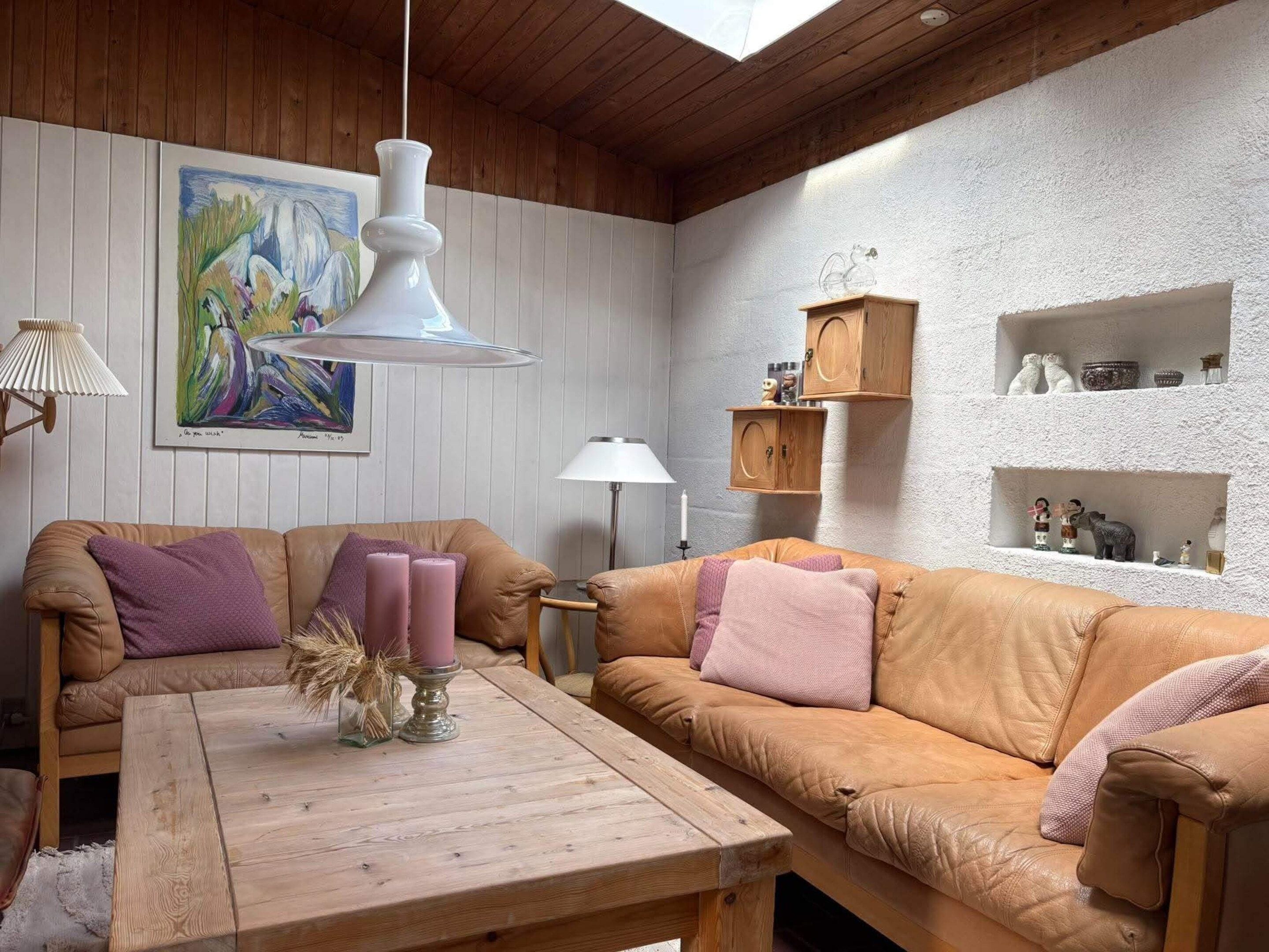 Una sala de estar acogedora con techo de madera, un cuadro en la pared y una lámpara colgante blanca.