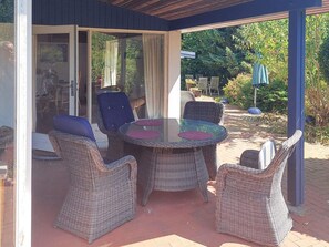 An outdoor patio with wicker furniture, a glass table, and a covered area with a view of the garden. - 4 Star Holiday Home in Hundested (Hundested)