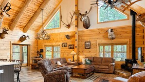 A log cabin interior with wooden walls, a high ceiling, and deer antlers mounted on the walls.
