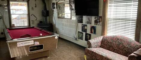 Una habitación con una mesa de billar, un sofá y una pared decorada con varias fotos y un televisor.