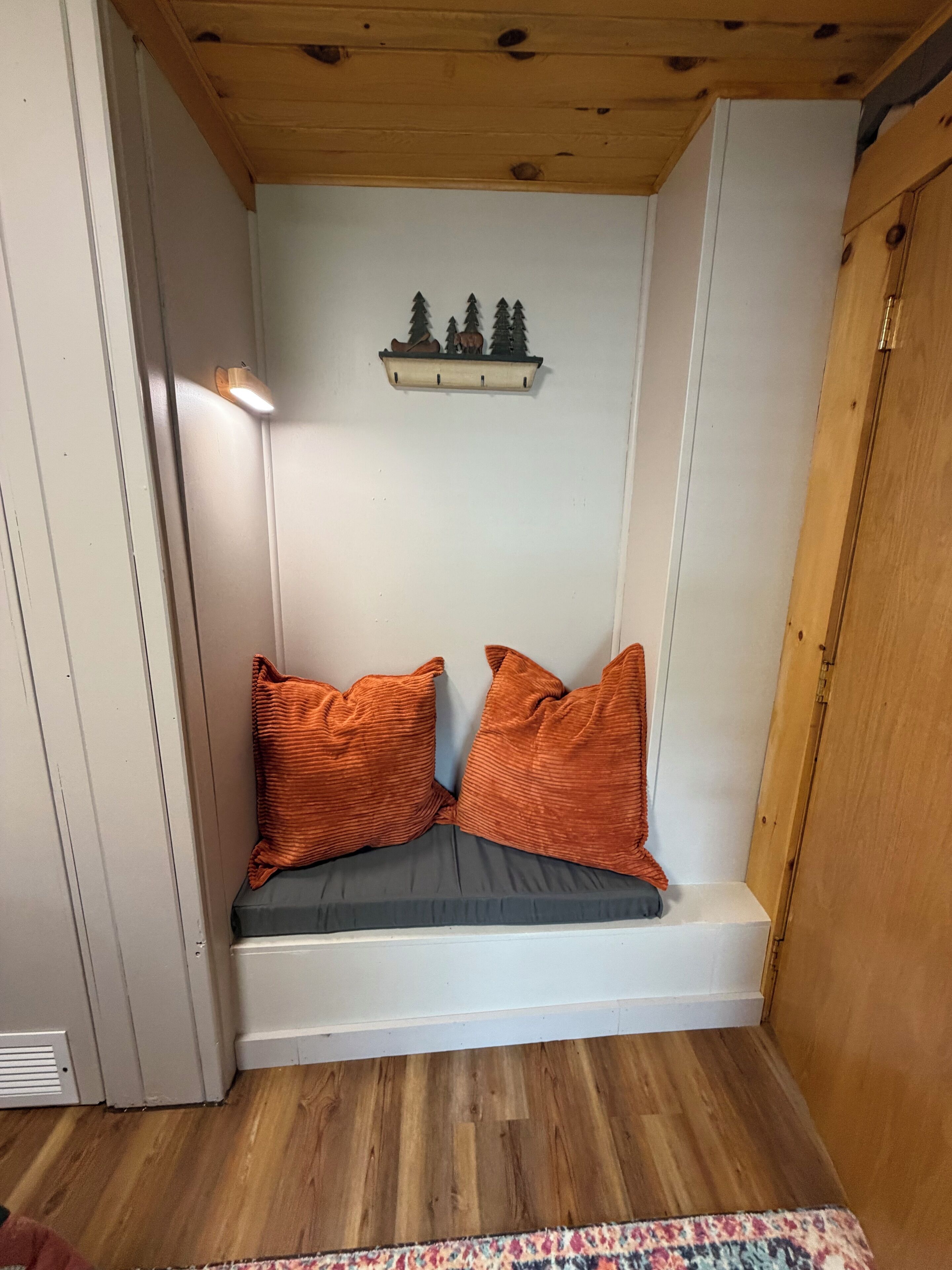 A corner room with a built-in bench, a shelf with a forest scene, and a wooden door.