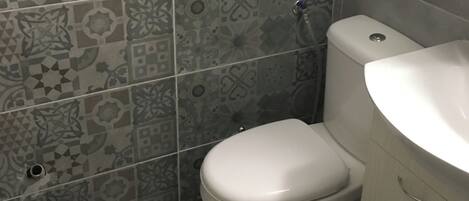 Une salle de bain comprenant des toilettes, un lavabo et une poubelle. Les murs sont recouverts de carreaux aux motifs décoratifs.