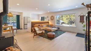 A modern living room with a fireplace, a sofa, a coffee table, and a dining area with a table and chairs. - Mountain Modern Retreat with Saltwater Hot tub and Cedar Sauna (Truckee)