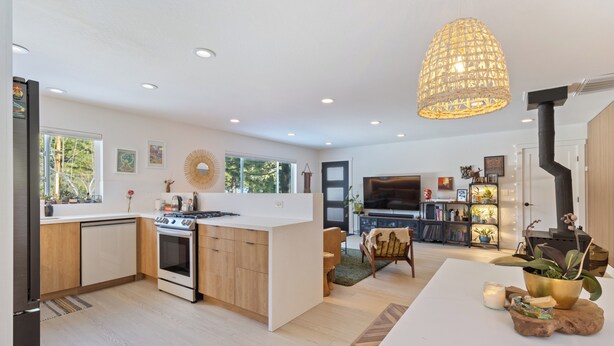 A modern kitchen with a central island, a dining area with a white table, and a living room with a TV and fireplace. - Mountain Modern Retreat with Saltwater Hot tub and Cedar Sauna (Truckee)