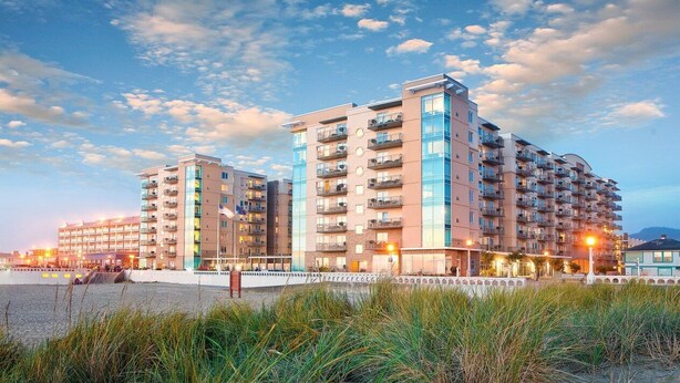 Un hotel de varios pisos con balcones, situado cerca de una playa con dunas de arena.