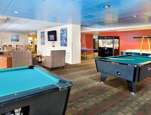 A pool table, another pool table, a television, and a claw machine in a room with striped chairs and a carpeted floor. - Seaside!! Condo with view, Balcony, Grill, just steps to the beach! (Seaside)
