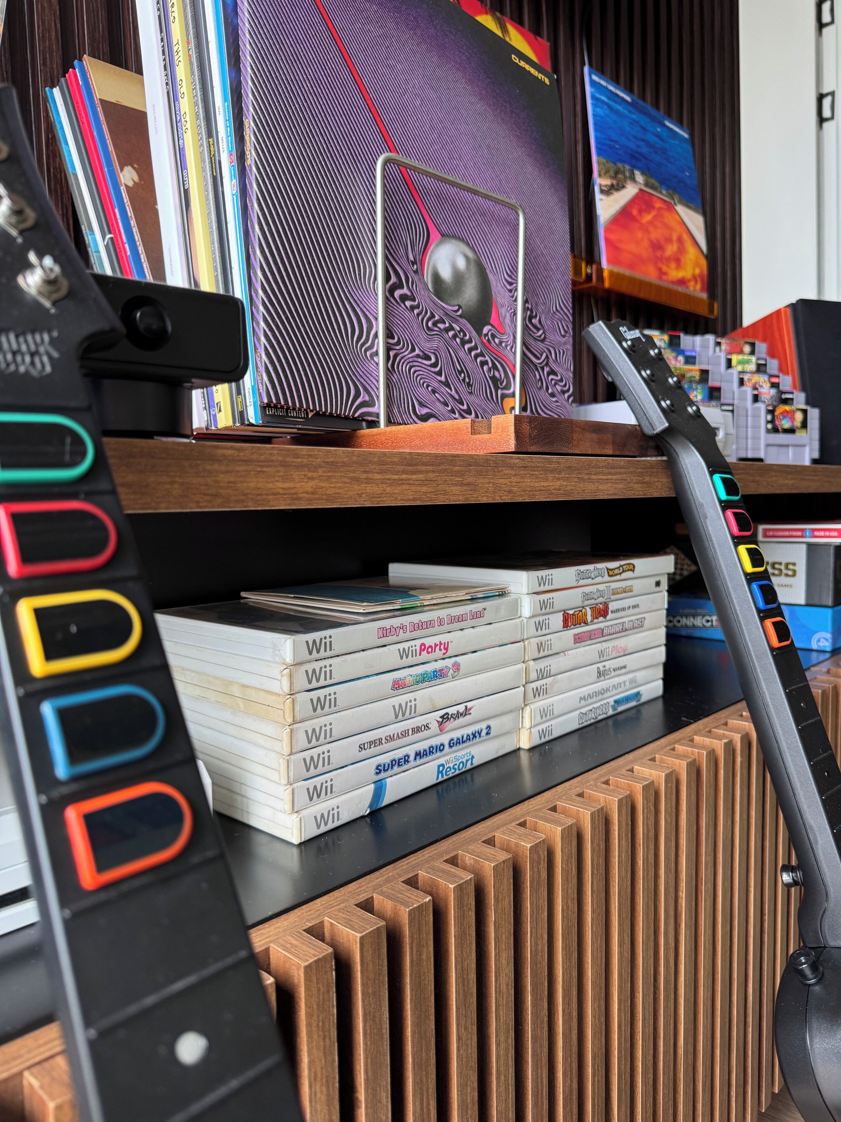 Un bureau en bois avec une console Wii, une guitare et une pile de boîtiers de jeux Wii.