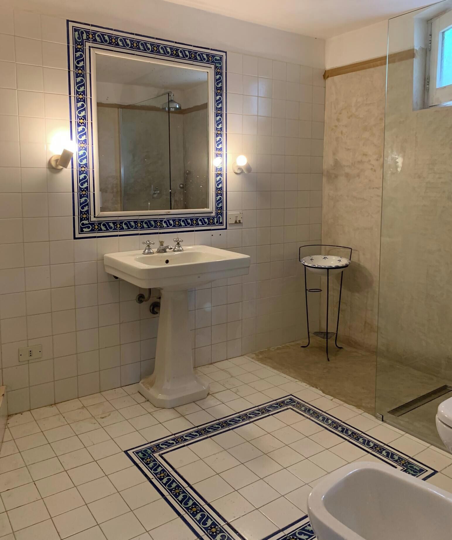 Een badkamer met een wit wastafelmeubel, een spiegel met decoratieve lijst, een klein rond tafeltje en een bad.
