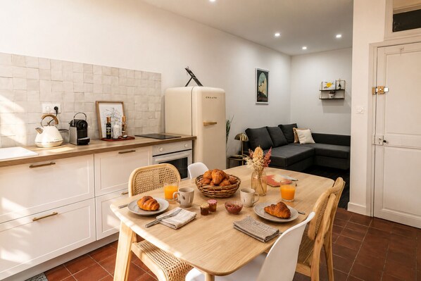 A modern kitchen with a dining table set for breakfast, a refrigerator, and a living area with a sofa.