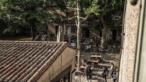 A courtyard with stone flooring, outdoor seating, and a building with a tiled roof.
