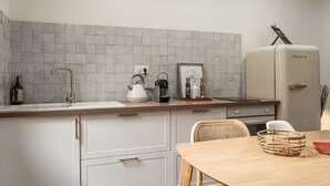 A kitchen with white cabinets, a sink, a kettle, a coffee maker, and a refrigerator.