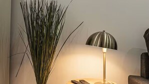 A lamp with a metallic shade and a round table with a remote control.