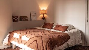A bedroom with a bed, a wall-mounted lamp, and decorative pillows.