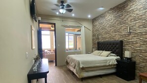 Un dormitorio con cama, mesita de noche, escritorio, ventilador de techo y pared de piedra.