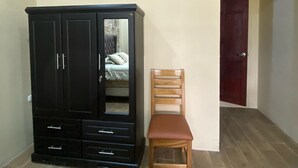 Una habitación con piso de madera, un armario negro con cajones, una silla de madera y una puerta.