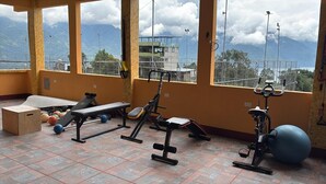 Un gimnasio con equipo de ejercicio, una banca y vistas a montañas a través de amplias ventanas.