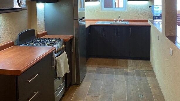 Una cocina moderna con gabinetes oscuros, una campana de acero inoxidable, estufa a gas e iluminación colgante.