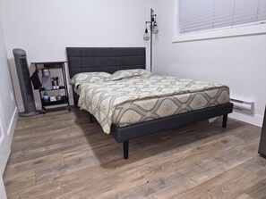 Un dormitorio con cama, mesita de noche, calefactor y lámpara de pie.