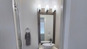 Ein Badezimmer mit einem weißen Waschbecken, dunklen Schränken, einem großen Spiegel und einer Duschkabine.