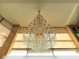 Un candelabro grande y ornamentado cuelga del techo en una habitación espaciosa con ventanas amplias y una paleta de colores neutros.