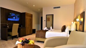 Habitación de hotel con cama, escritorio, televisión, espejo adosado a la pared y una cesta de frutas.